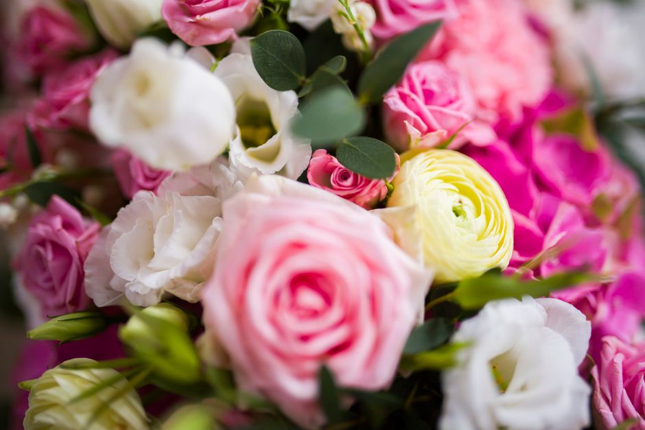A vibrant floral arrangement featuring a variety of fresh flowers including pale pink roses, white lisianthus, bright yellow ranunculus, and clusters of pink spray roses, all interspersed with green e