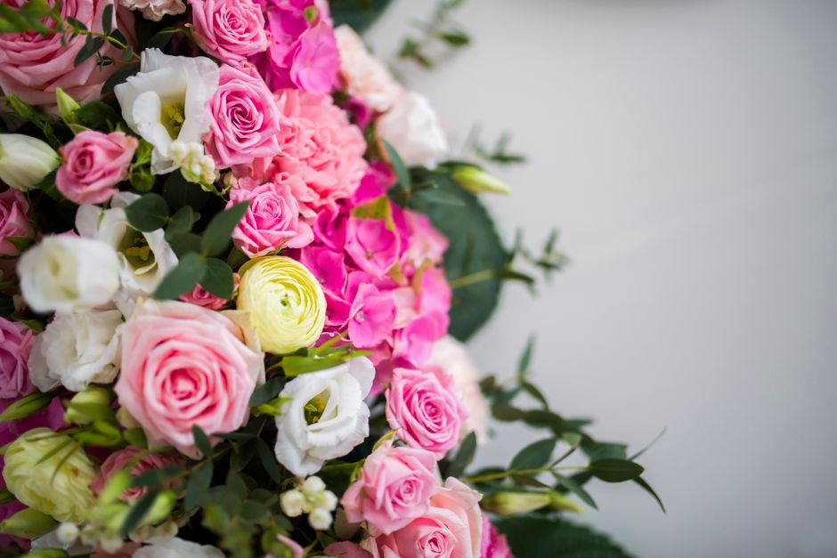 A detailed close-up of a floral arrangement featuring a variety of fresh flowers including soft pink roses, white lisianthus, and bright yellow ranunculus, intricately arranged with lush green foliage